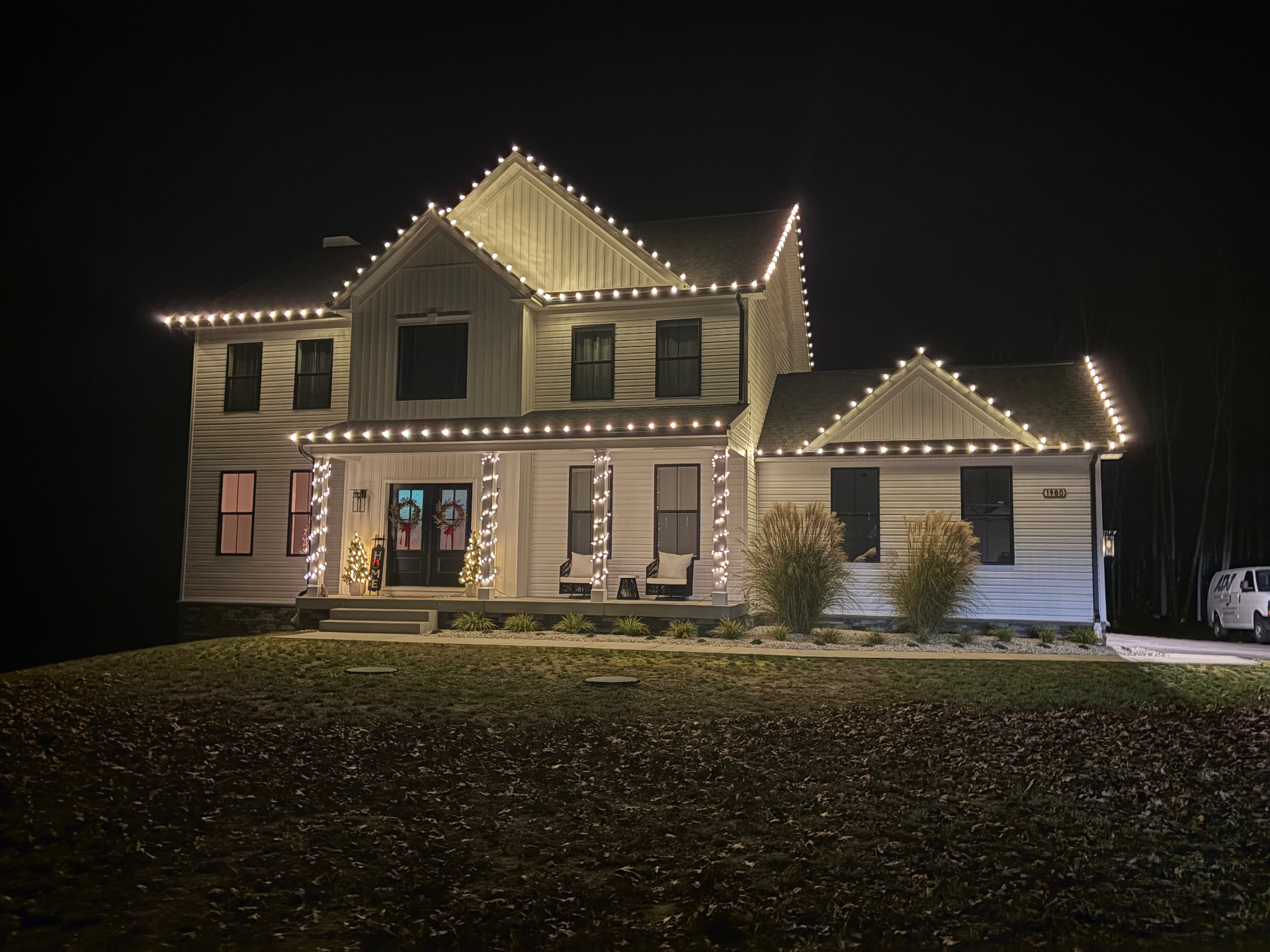 Warm white lights along every roofline and porch column of a white farmhouse